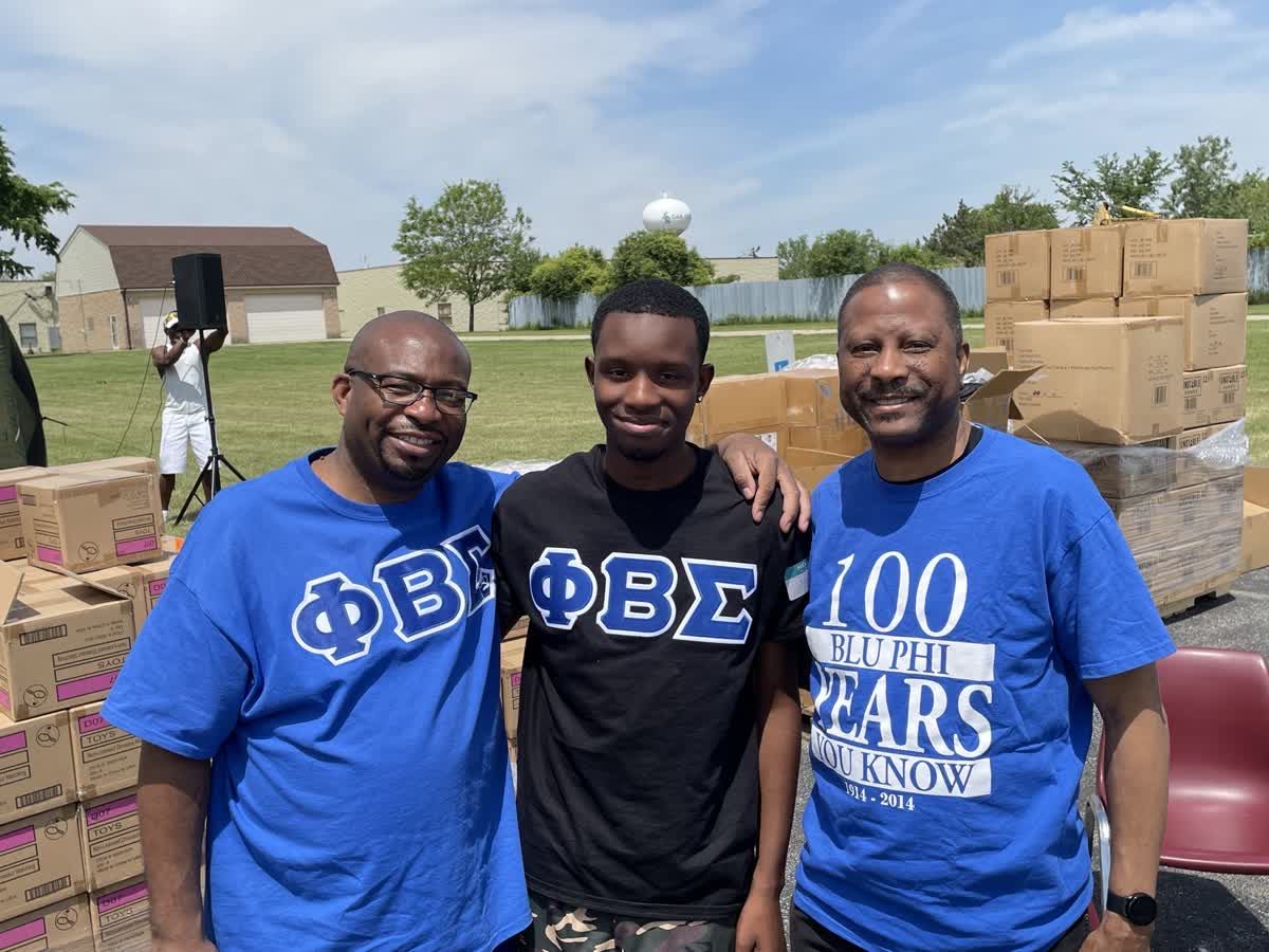 Three brothers in Phi Beta Sigma shirts at a community food distribution